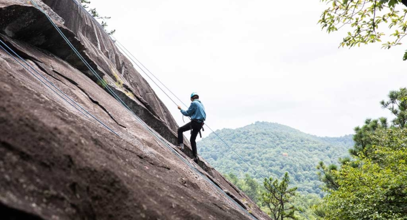 A person wearing safety gear is secured by ropes as they climb up a rock incline. 
